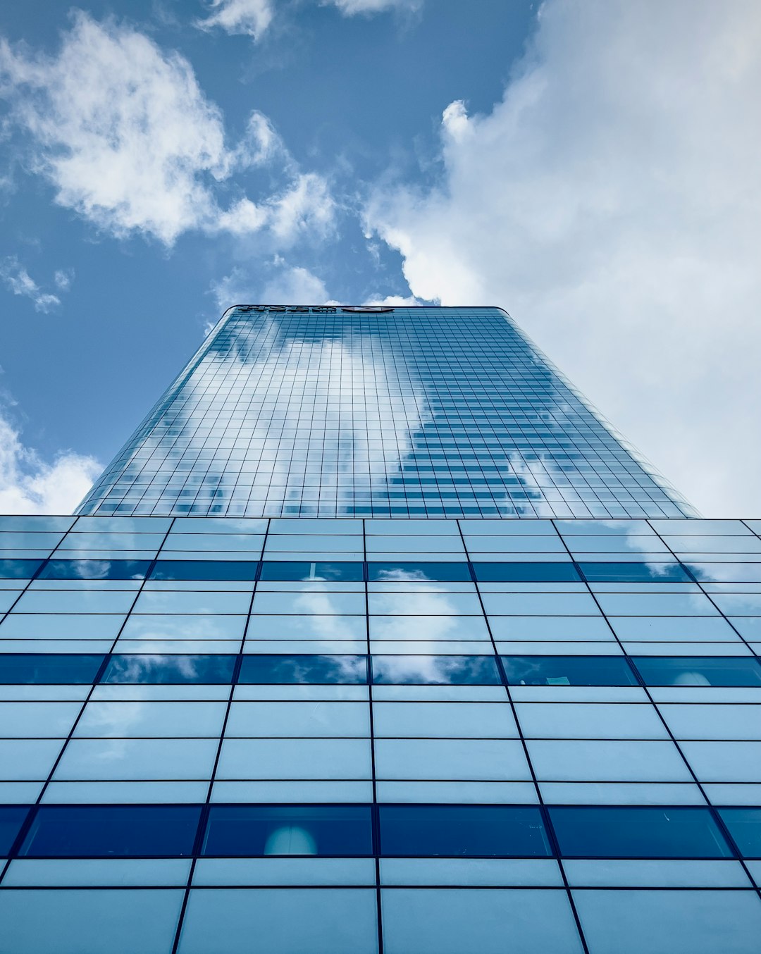 Fluffy clouds reflected in the curtain wall glass covering a tall building in London’s Canary Wharf business district